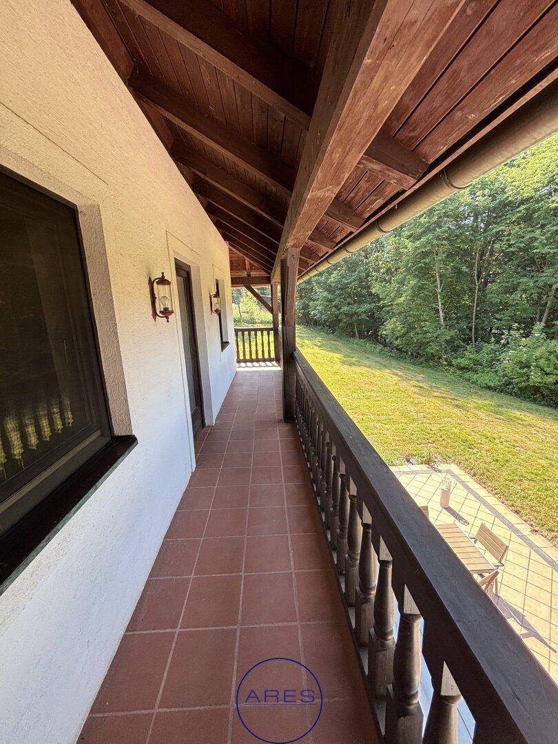 Überdachter Balkon mit Terrakottafliesen und Blick ins Grüne.