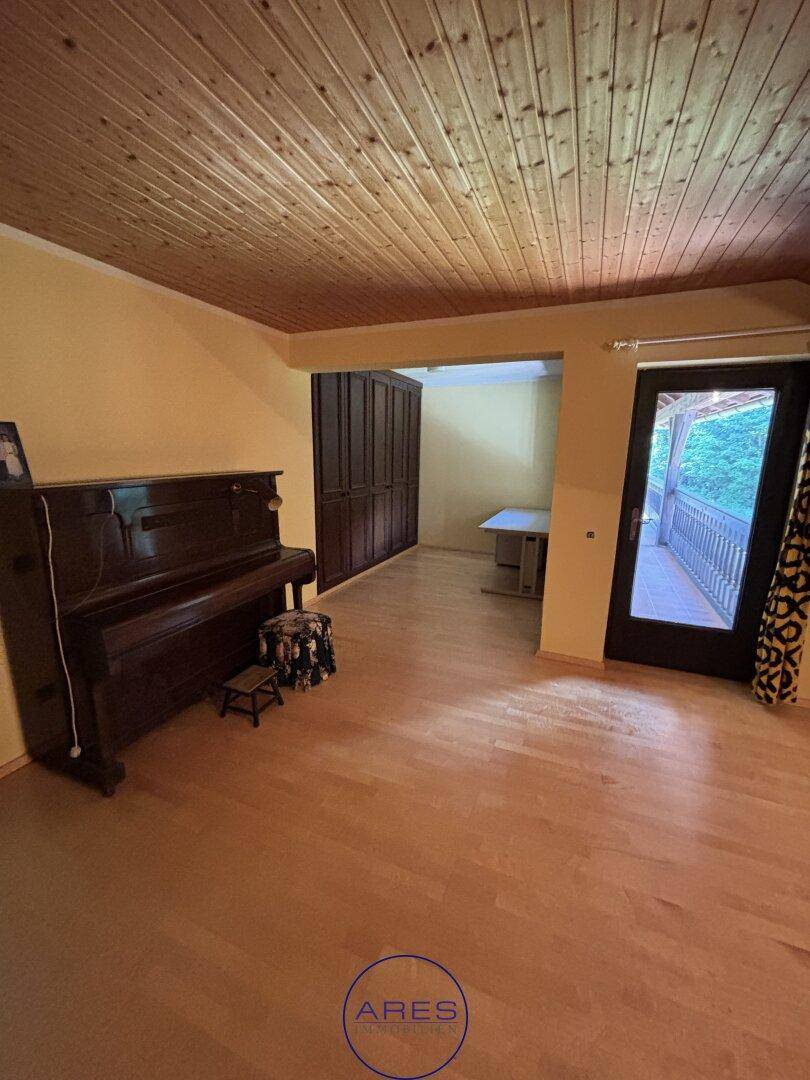 Geräumiger Raum mit Holzdecke, Holzboden und Klavier.