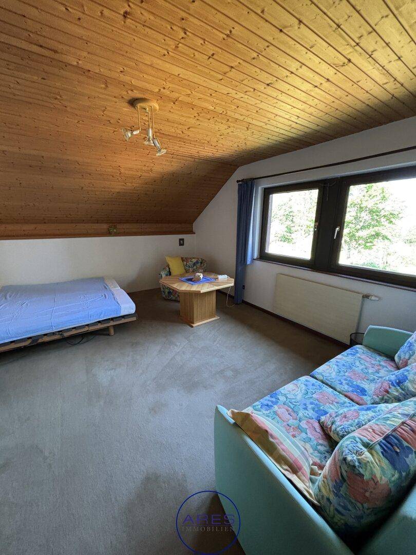 Gemütliches Schlafzimmer im Dachgeschoss mit Holzdecke und Sitzbereich.