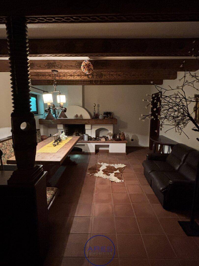Rustikaler Wohn-Essbereich mit Kamin, Holzbalken und großem Esstisch.