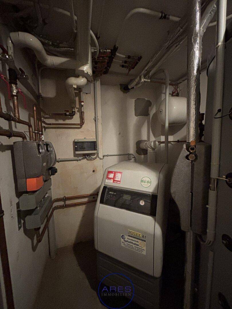 Heizungsraum im Keller mit einem modernen Heizkessel und zahlreichen Rohrleitungen.