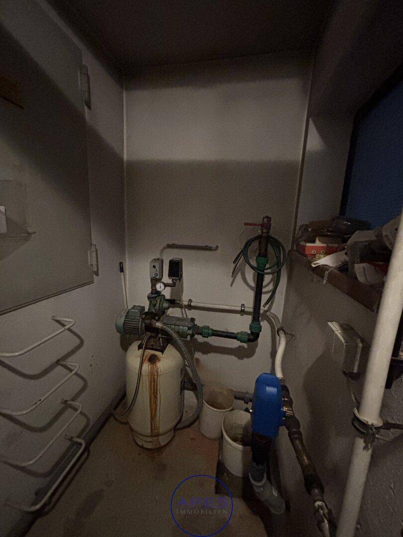 Kleiner Technikraum mit Wasserpumpe und verschiedenen Rohrleitungen.