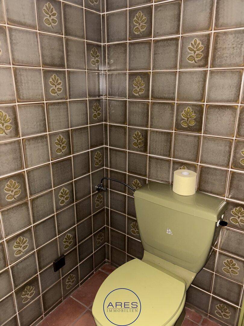WC mit auffälligen grünen Fliesen und einer passenden Toilette im Retro-Stil.