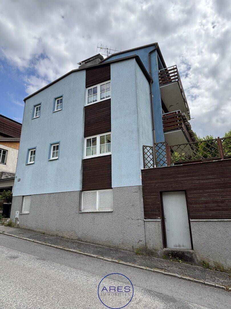 Seitenansicht des Wohnhauses mit hellblauer Fassade, weißen Fenstern und braunen Holzelementen.