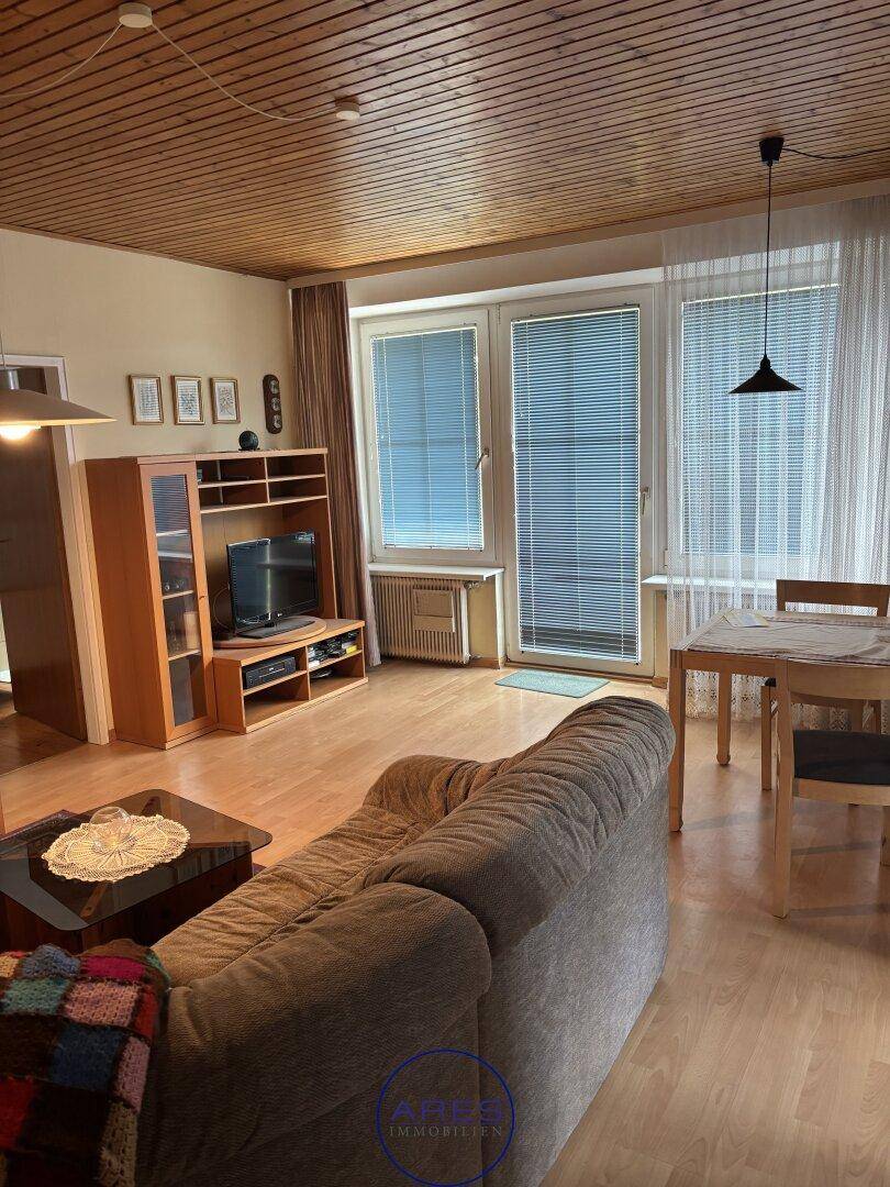 Gemütliches Wohnzimmer mit Holzdecke, Parkettboden und einem Essbereich am Fenster.