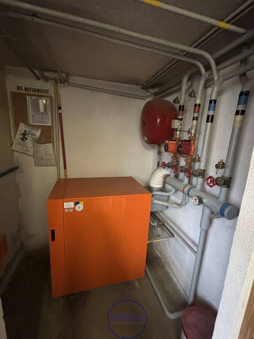 Heizungsraum mit einem orangefarbenen Heizkessel und sichtbaren Rohrleitungen.