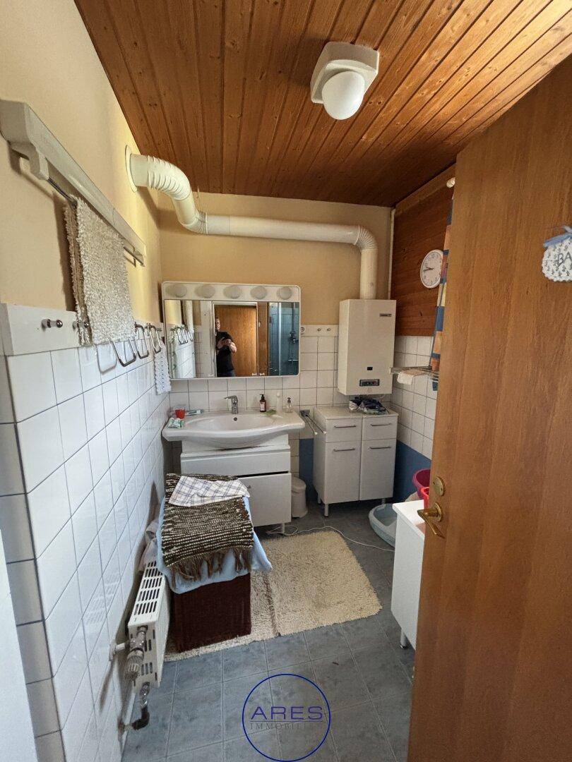 Badezimmer mit Holzdecke, Waschbecken, Spiegel und weißen Wandfliesen.