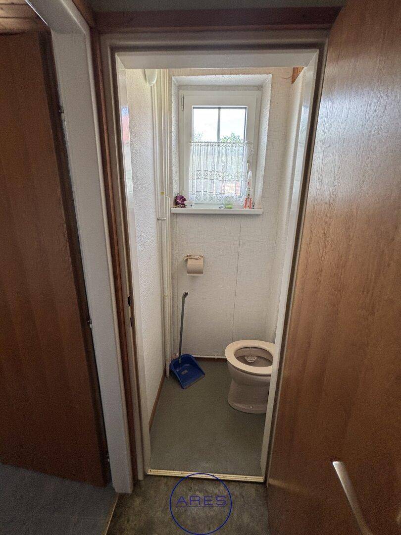 Schmale separate Toilette mit Fenster und einfachen weißen Wänden.