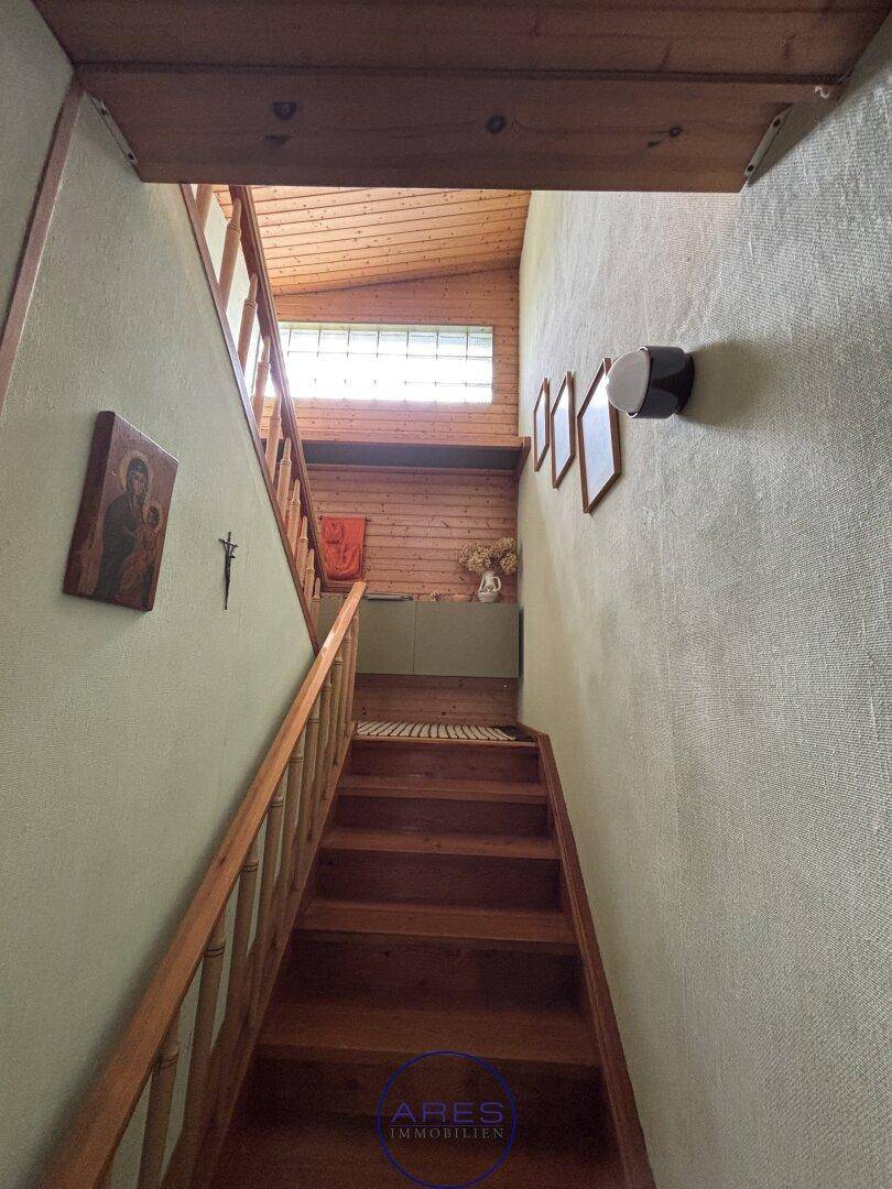 Holztreppe führt nach oben, mit hellgrünen Wänden und einem Fenster im oberen Bereich.