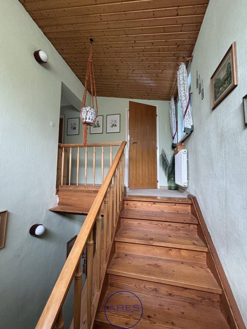 Holztreppe mit Geländer und Holzdecke, die zu einem Flur führt.