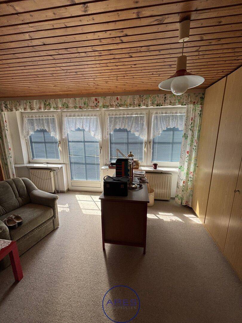 Helles Zimmer mit Teppichboden, Holzdecke und mehreren Fenstern.