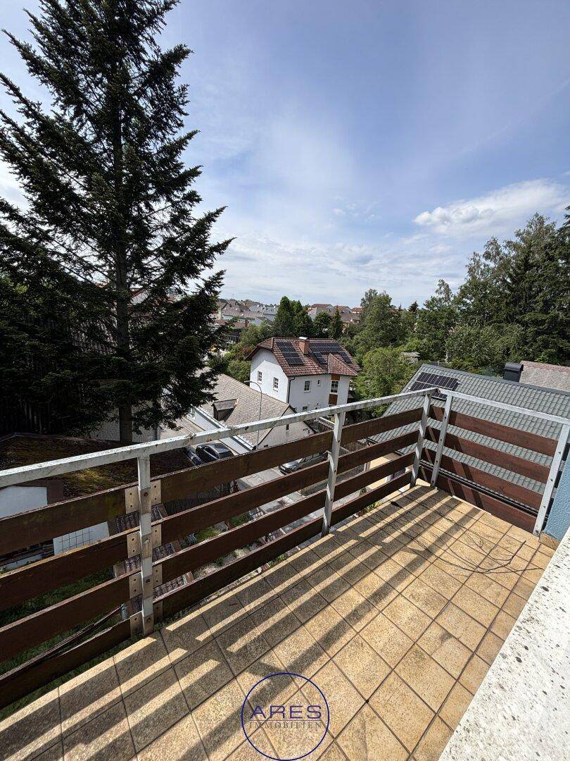 Balkon mit Fliesenboden und weitem Blick über die Dächer und grüne Umgebung.