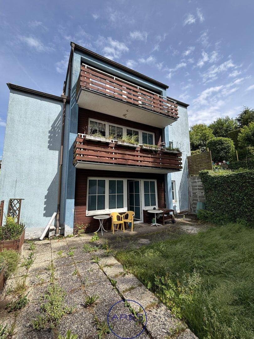 Rückseite des Hauses mit Balkonen und einer Terrasse, die in einen Garten übergeht.