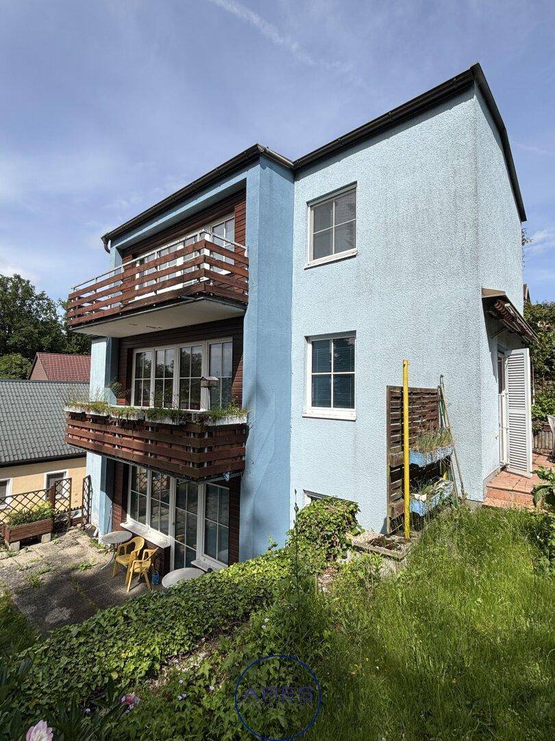 Seitenansicht des Hauses mit Balkonen und einem grünen Gartenbereich im Vordergrund.