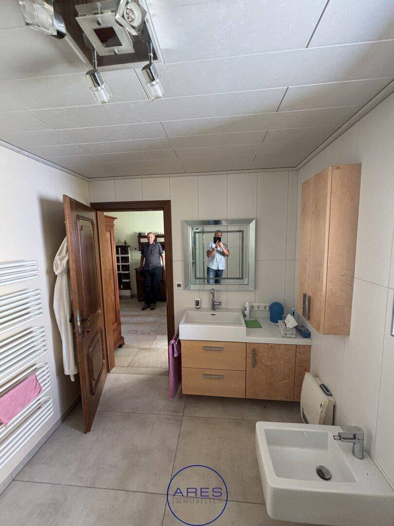 Badezimmer mit Waschtisch, Spiegelschrank und Zugang zu einem weiteren Raum.