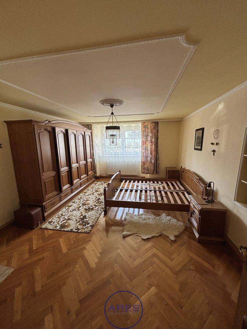 Schlafzimmer mit Fischgrätparkett, großem Holzschrank und Stuckdecke.