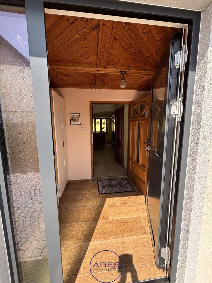 Eingangsbereich mit Holzbalkendecke, Fliesenboden und offener Tür zum Außenbereich.