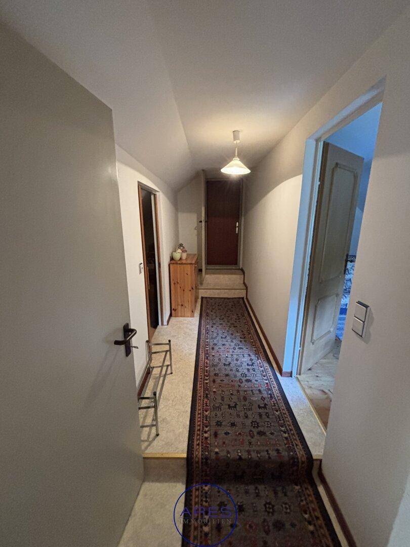 Langer Flur im Dachgeschoss mit Teppichläufer und schrägen Wänden.