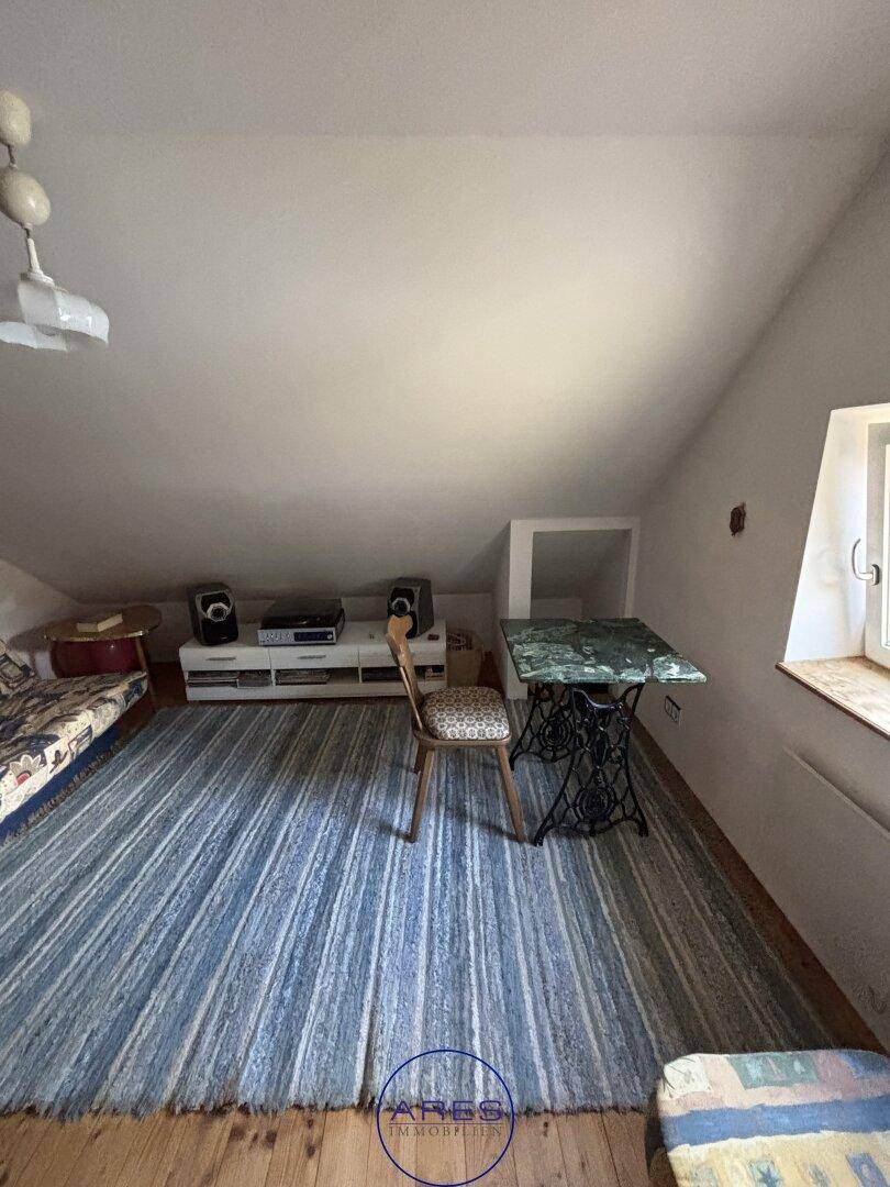 Dachzimmer mit Holzboden, Teppich und Fenster für natürliches Licht.