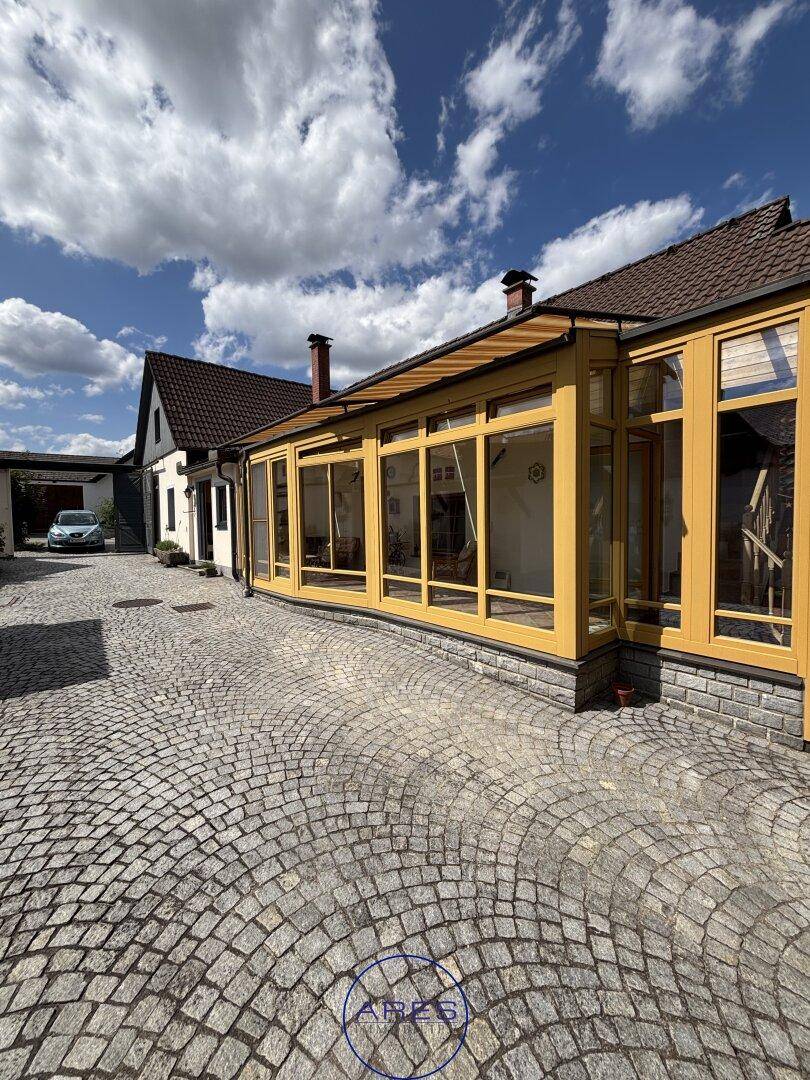 Außenansicht des Wintergartens mit gepflastertem Hof und weiteren Gebäuden.