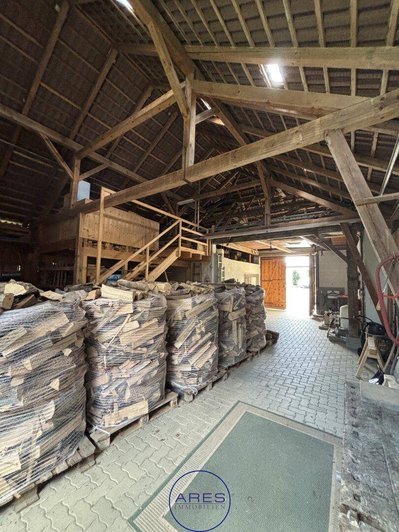 Große Scheune mit Holzstapeln, Holzbalken und Zugang zum Außenbereich.