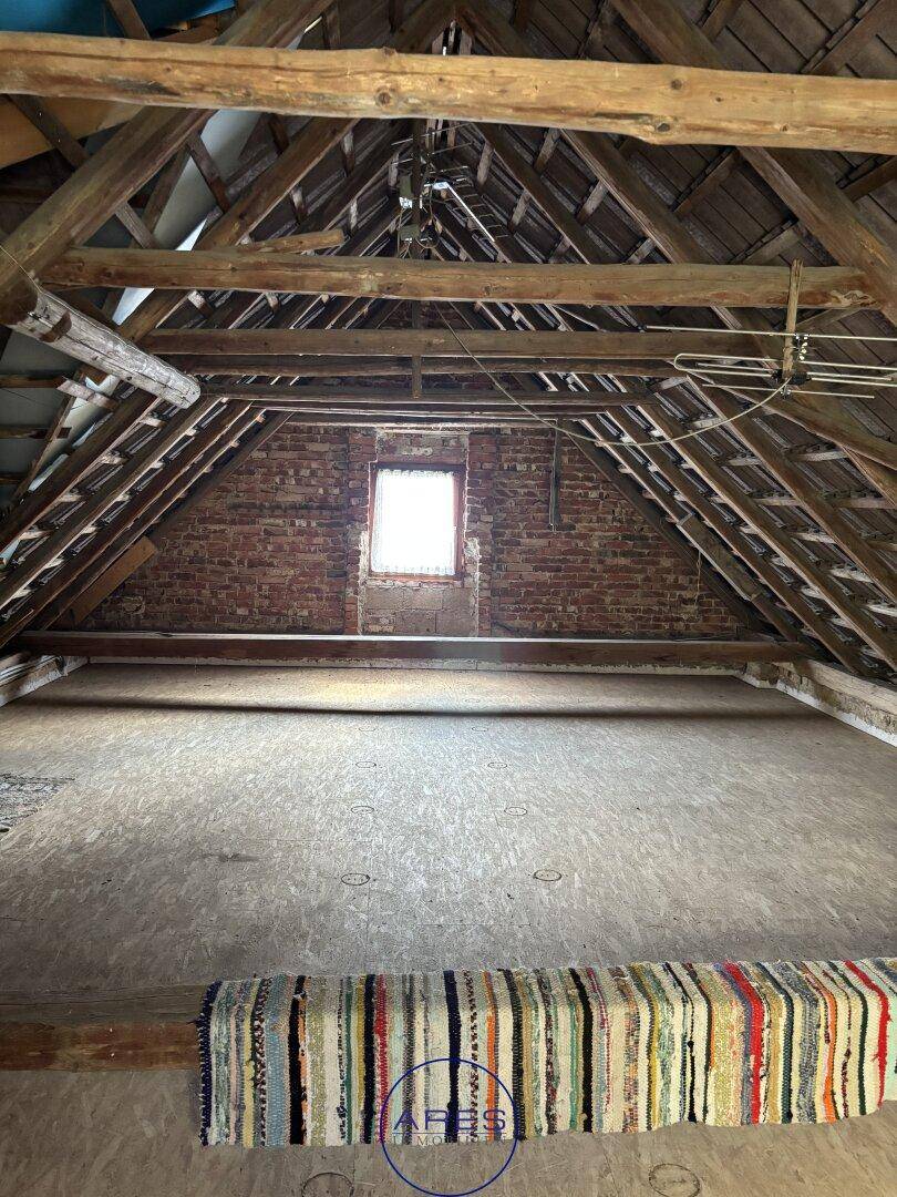 Geräumiger Dachboden mit sichtbaren Holzbalken und einem kleinen Fenster, das Tageslicht hereinlässt.