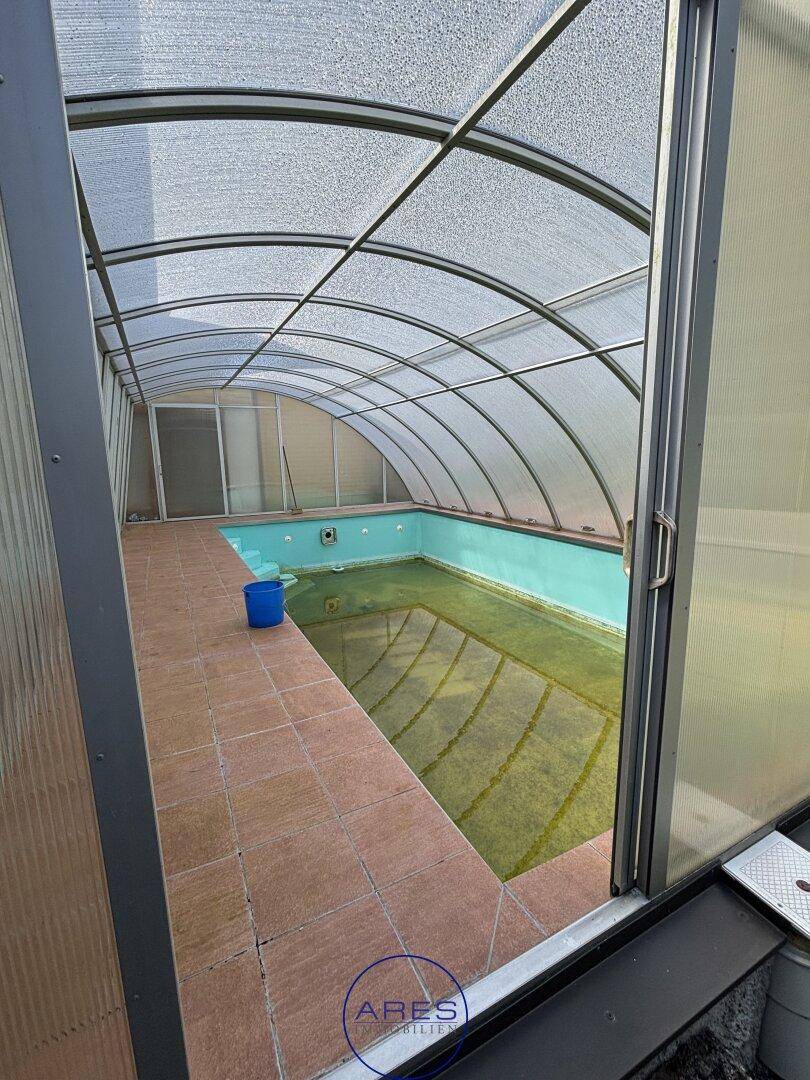 Überdachtes Schwimmbad mit gewölbtem Dach und gefliestem Boden, bereit zur Nutzung.
