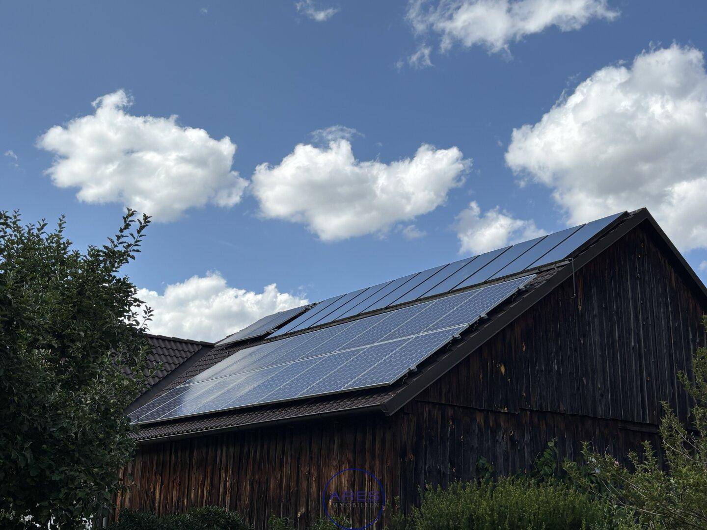Rustikales Holzgebäude mit Photovoltaikanlage auf dem Dach unter blauem Himmel.