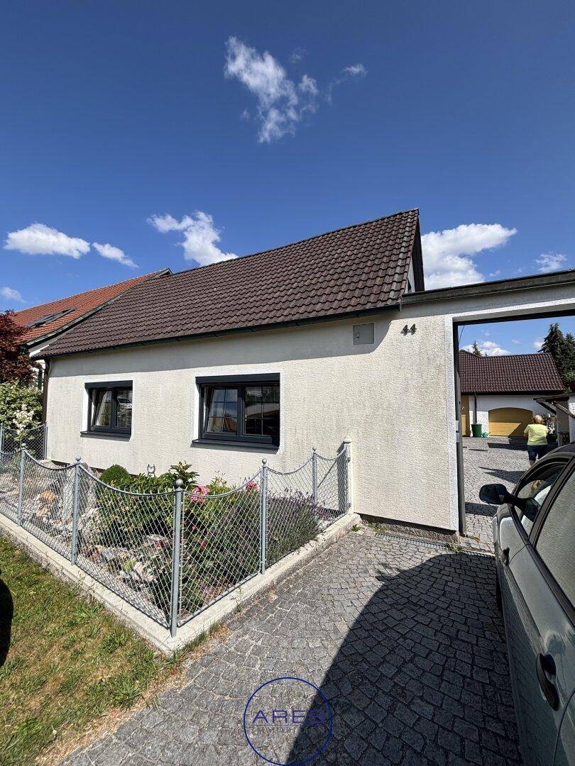 Kleines Haus mit gepflasterter Einfahrt und einem umzäunten Vorgarten unter blauem Himmel.
