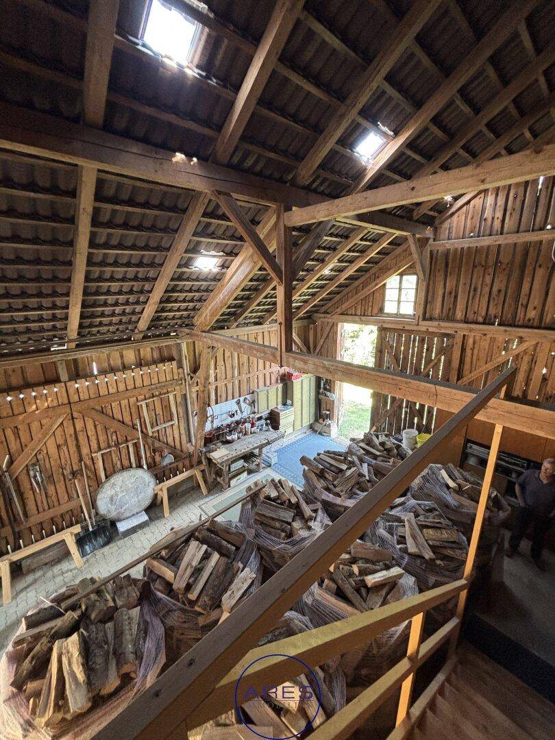 Geräumiger Scheuneninnenraum mit gestapeltem Brennholz, sichtbaren Holzbalken und hoher Decke.