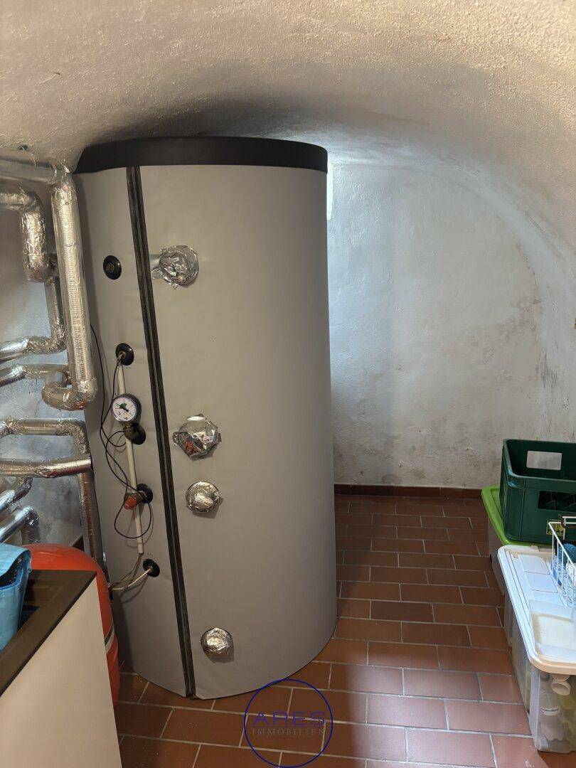 Großer Warmwasserspeicher oder Boiler in einem Kellerraum mit gewölbter Decke und Ziegelboden.