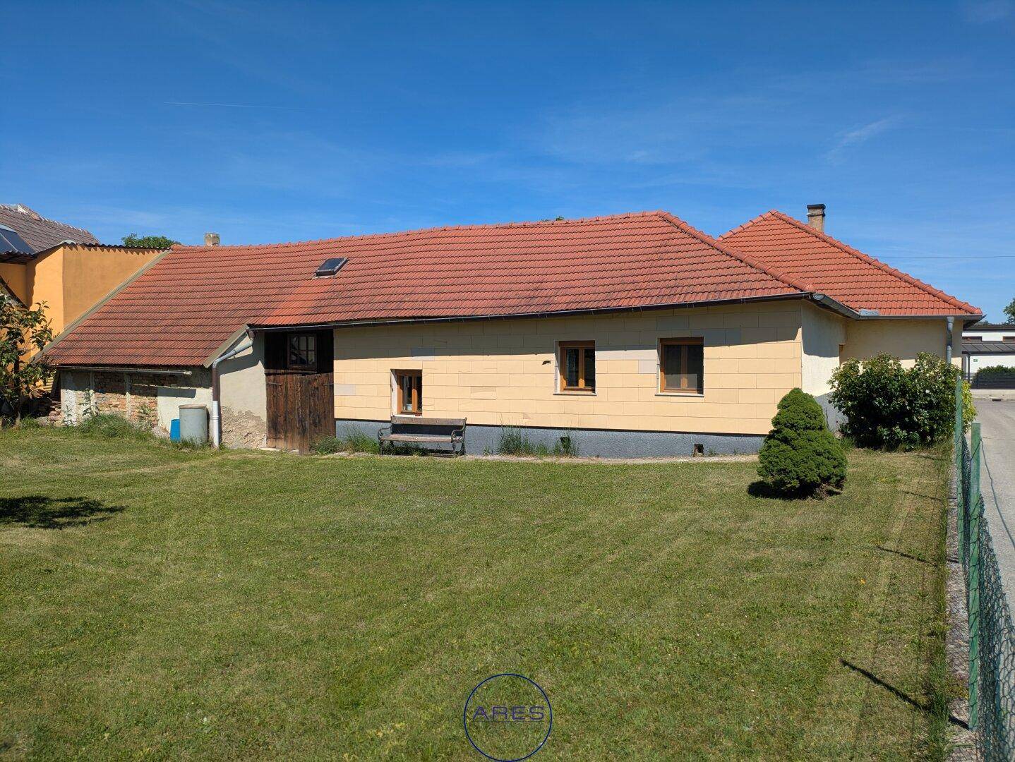 Rückansicht des Hauses mit großem grünen Rasen und rotem Ziegeldach unter blauem Himmel.