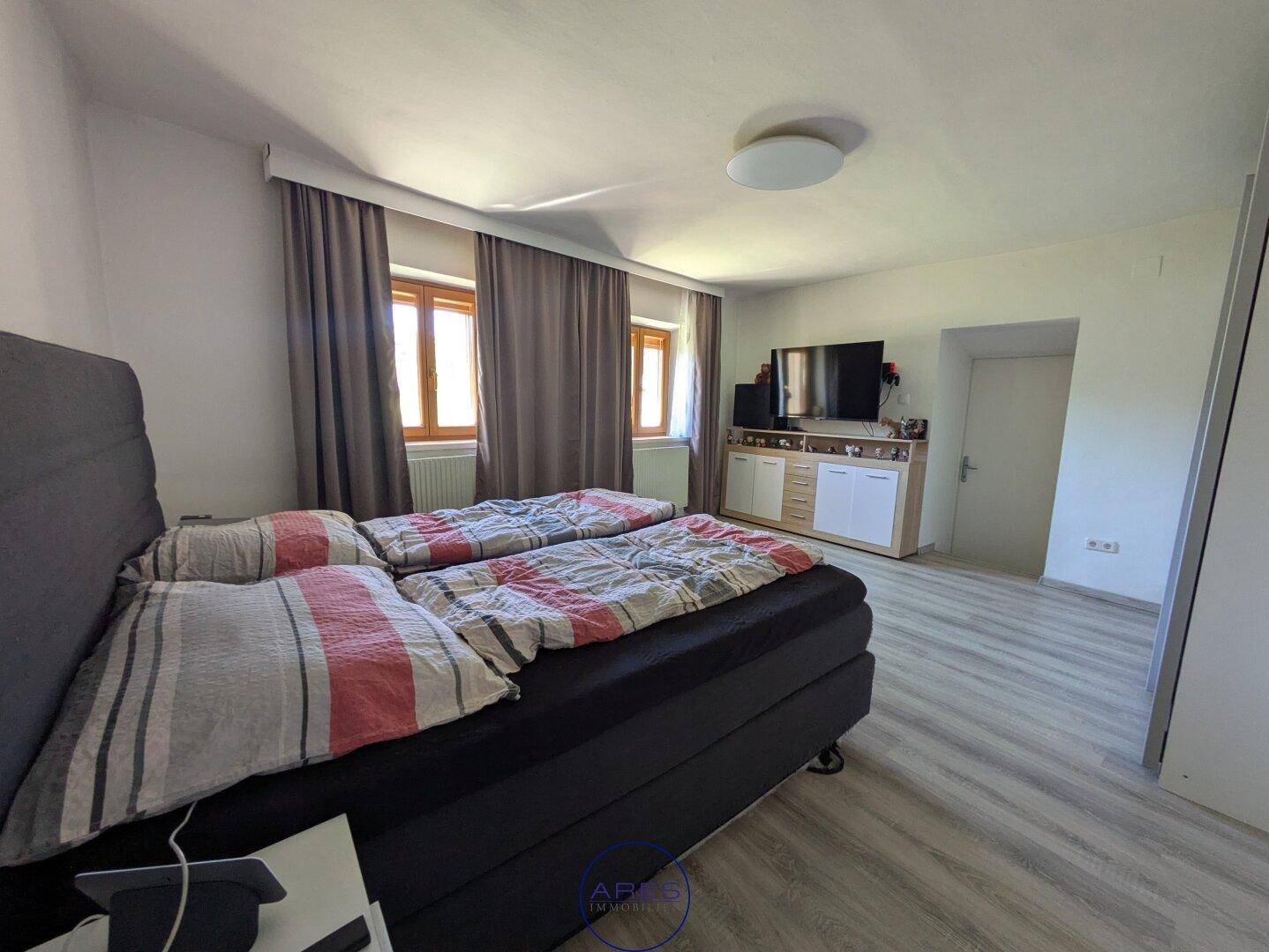 Gemütliches Schlafzimmer mit zwei Betten, Laminatboden und Fenstern mit Vorhängen.