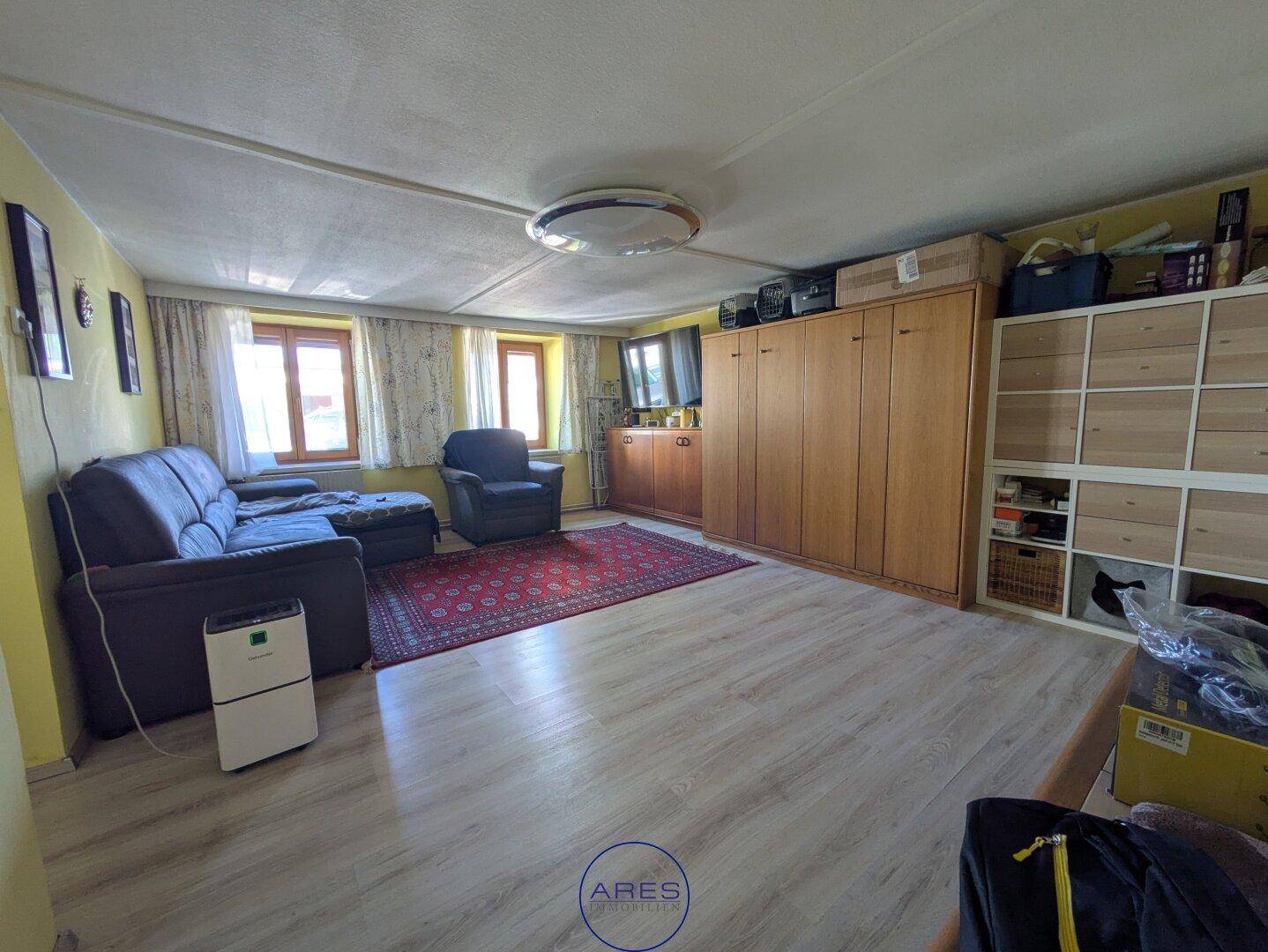 Geräumiges Wohnzimmer mit Sofa, Sessel, Holzschrank und Laminatboden.