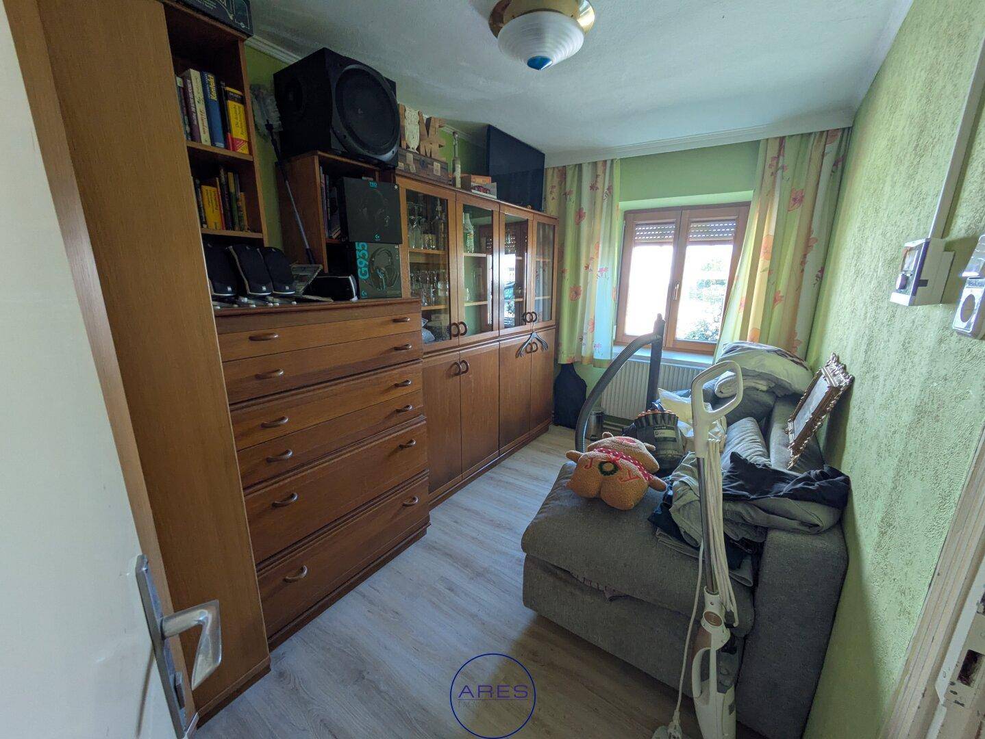 Kleines Zimmer mit Sofa, Holzmöbeln und grüner Tapete, möglicherweise ein Gästezimmer.