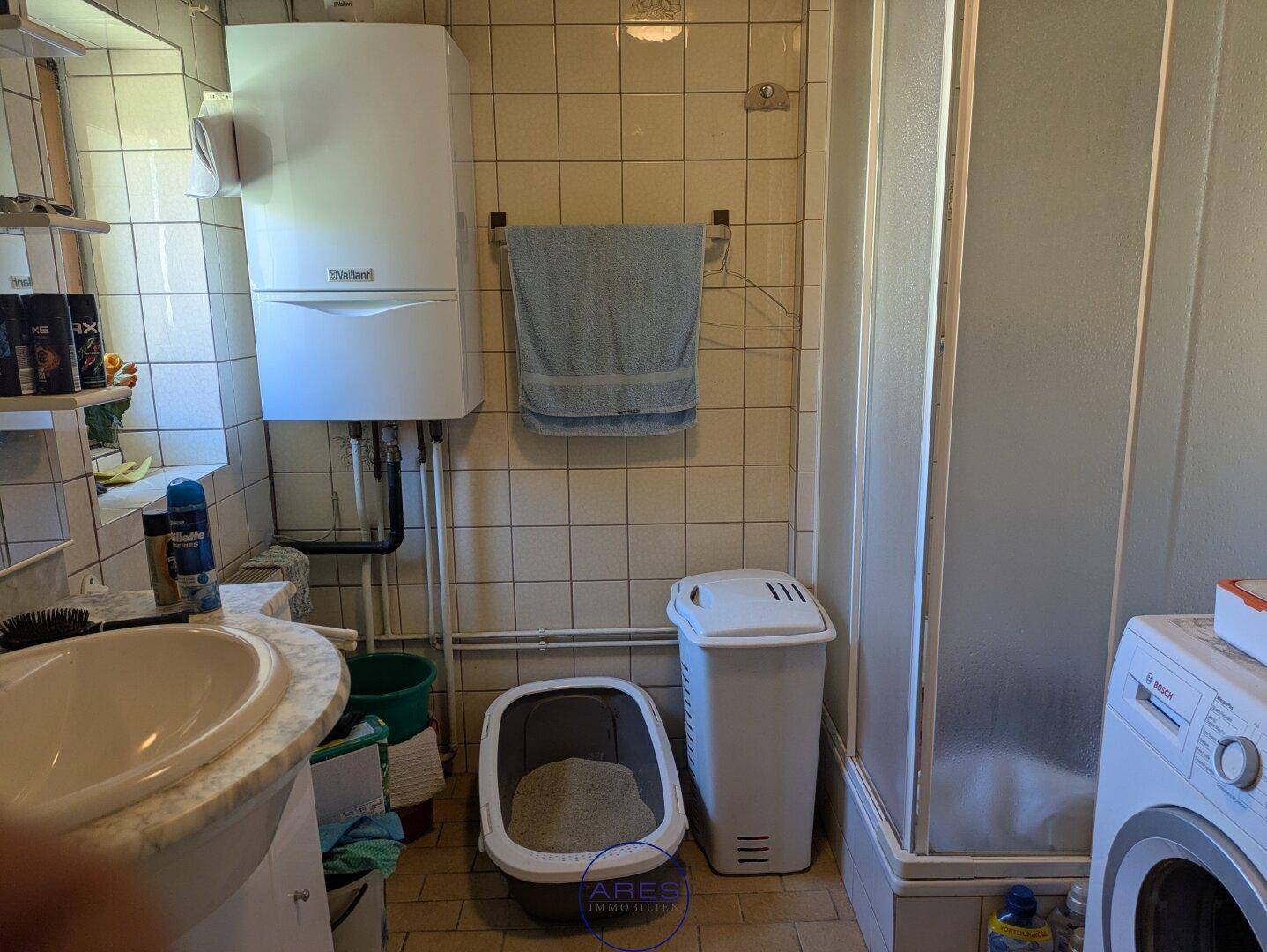 Badezimmer mit Dusche, Waschbecken, WC, Waschmaschine und Gastherme.