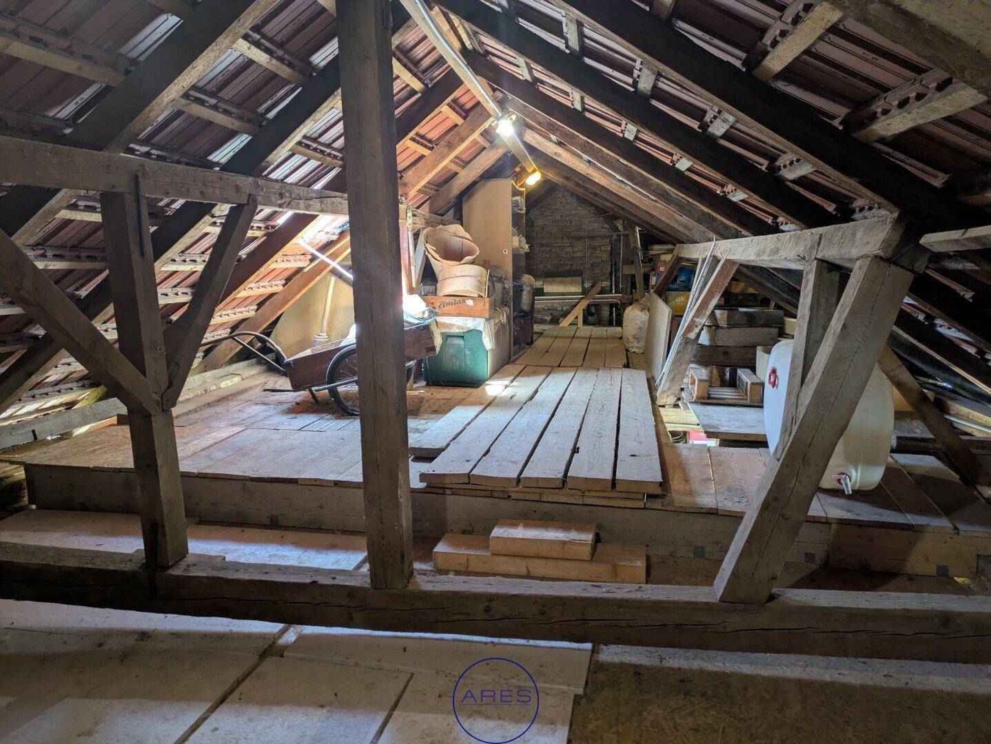 Weiterer Blick in den unausgebauten Dachboden mit Holzkonstruktion und gelagerten Gegenständen.