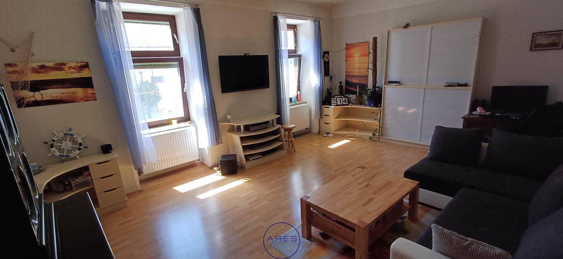 Helles Wohnzimmer mit Holzfußboden, großen Fenstern und moderner Einrichtung.