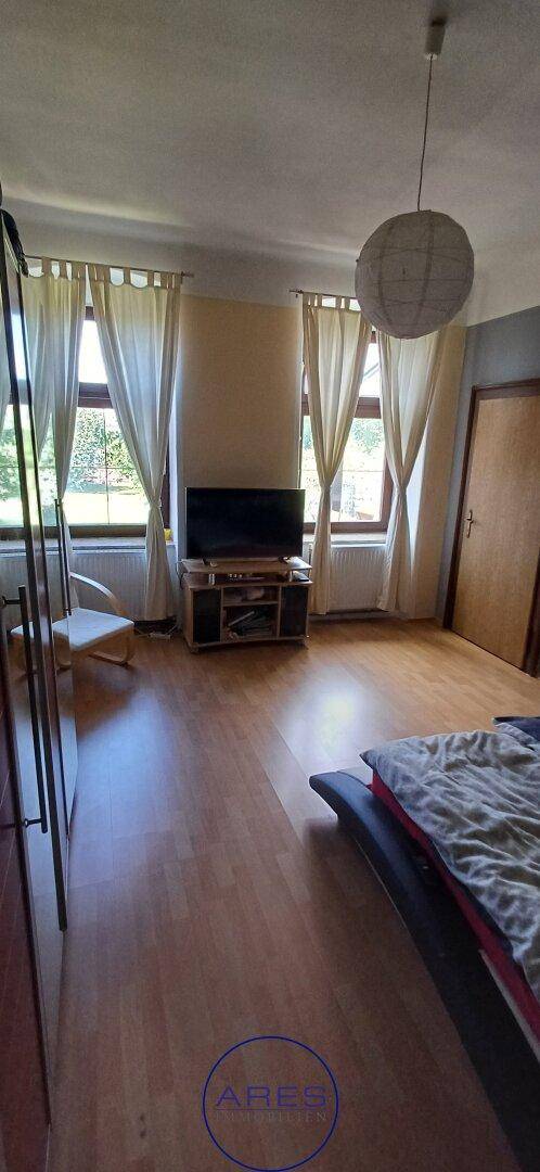 Schlafzimmer mit hellem Holzfußboden, großen Fenstern und Blick ins Grüne.