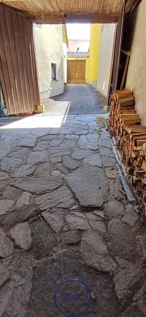 Gepflasterter Innenhof mit Natursteinplatten und gestapeltem Brennholz.