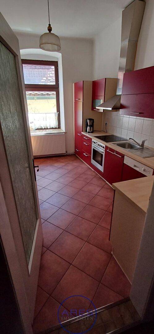 Küche mit roten Schränken, Fliesenboden und Fenster mit Blick nach draußen.