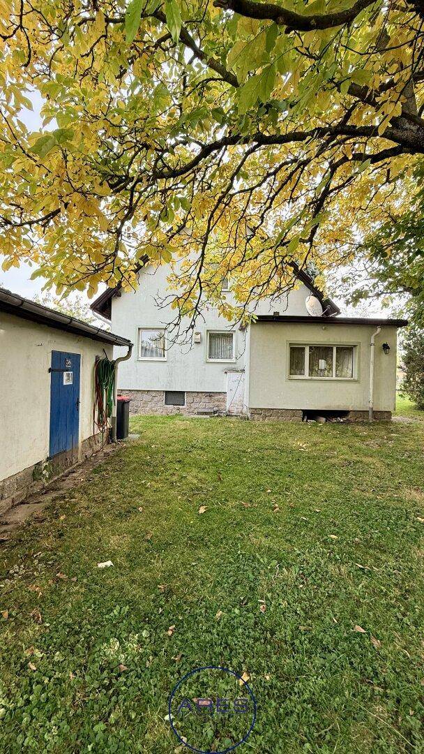 Rückseite des Hauses mit Nebengebäude und weitläufigem Rasen, umgeben von Bäumen mit Herbstlaub.