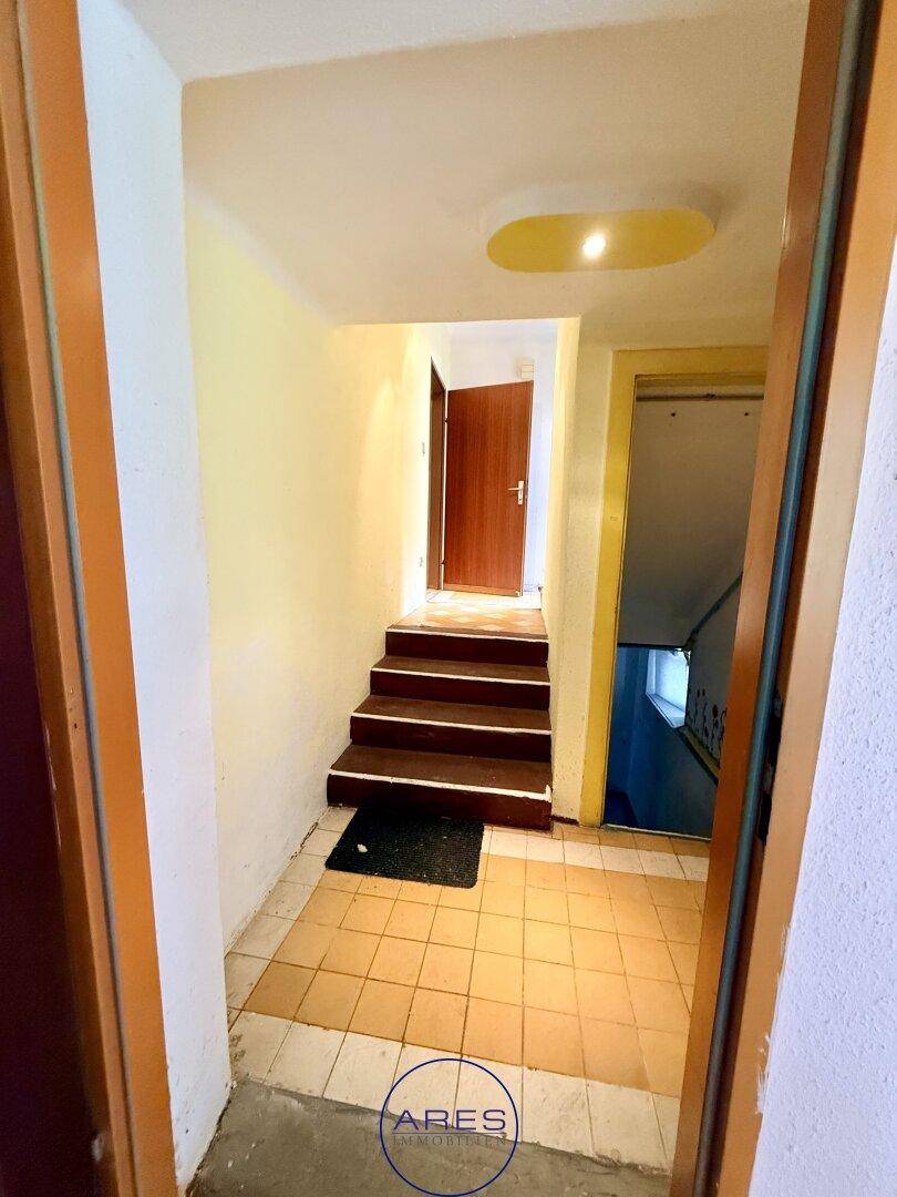 Eingangsbereich mit gefliestem Boden und Holztreppe, die in die oberen Stockwerke führt.