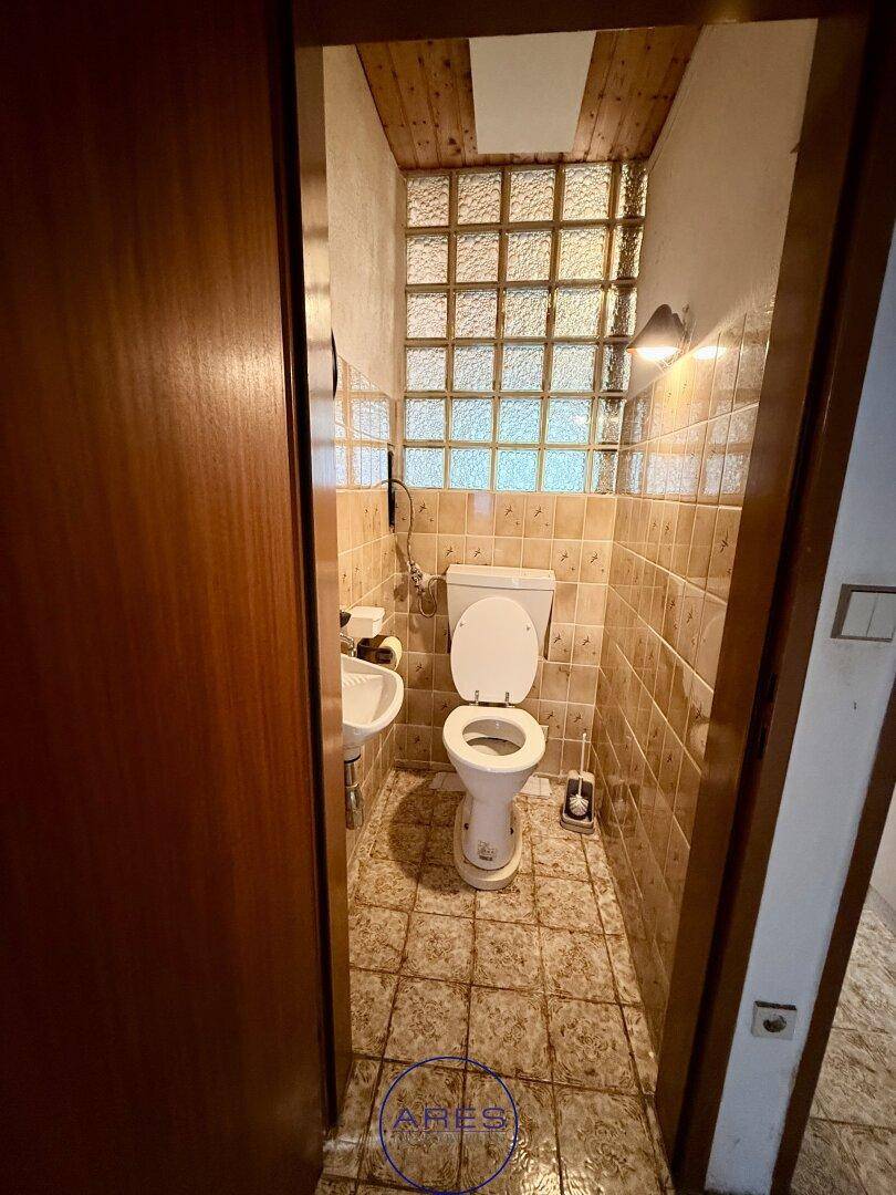 Kleines Gäste-WC mit gefliesten Wänden und Boden, Toilette und Waschbecken sowie Glasbausteinfenster.