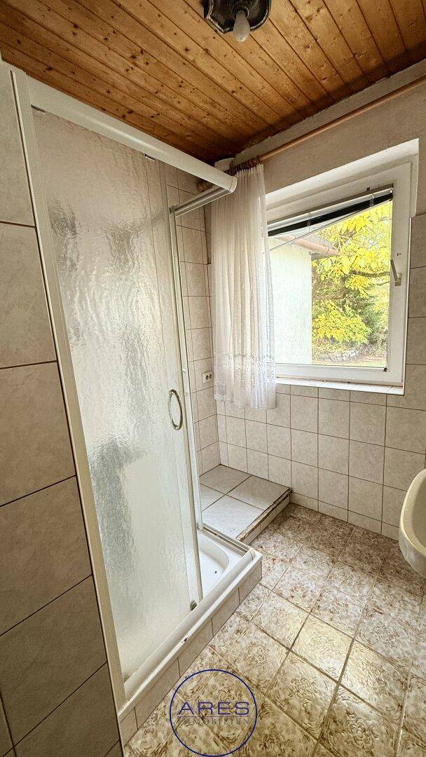 Badezimmer mit Duschkabine, gefliestem Boden und Wänden sowie einem Fenster und Holzdecke.