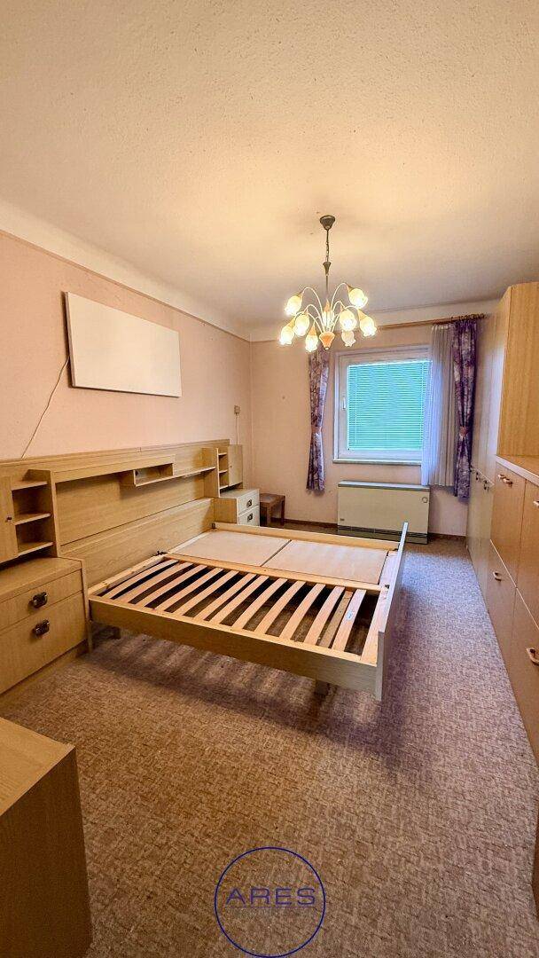 Schlafzimmer mit Holzbettenrahmen, passenden Holzschränken und Teppichboden, hell durch Fenster.