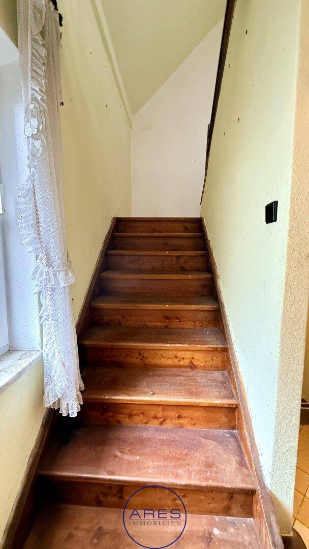 Rustikale Holztreppe führt in die oberen Stockwerke, mit einfacher Wandgestaltung und Fenster.