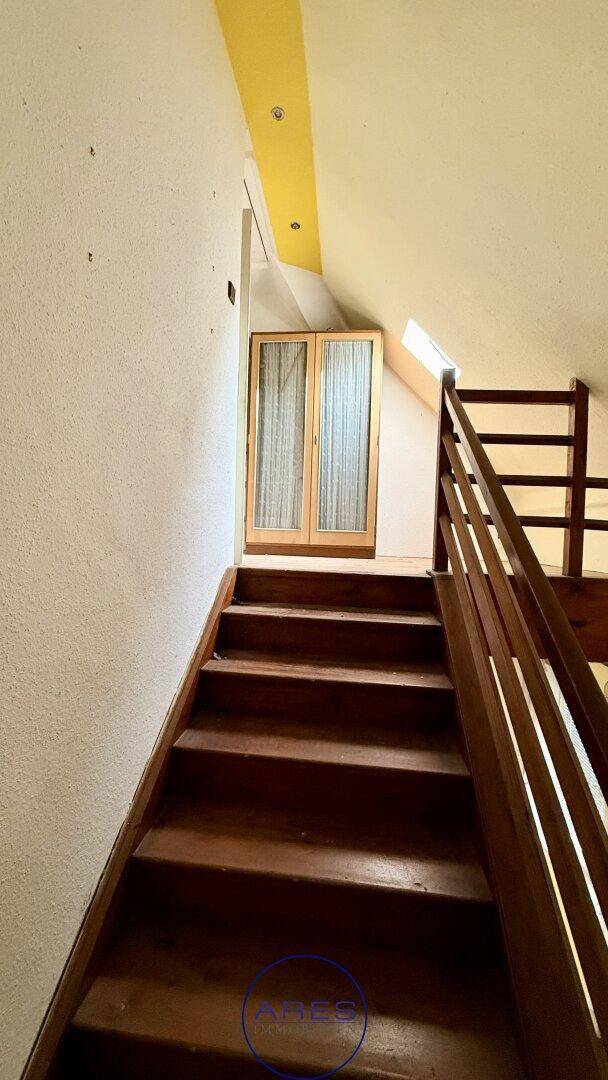 Holztreppe mit Holzgeländer führt nach oben, mit einem Fenster am Treppenabsatz für natürliches Licht.
