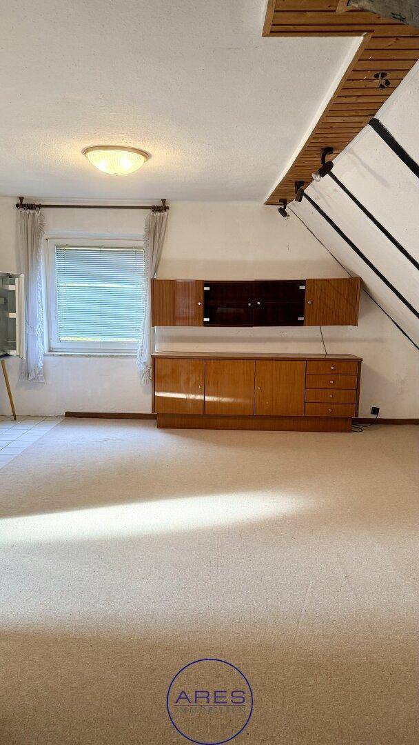Heller Dachbodenraum mit Teppichboden, Fenster und Holzmöbeln unter einer Dachschräge.