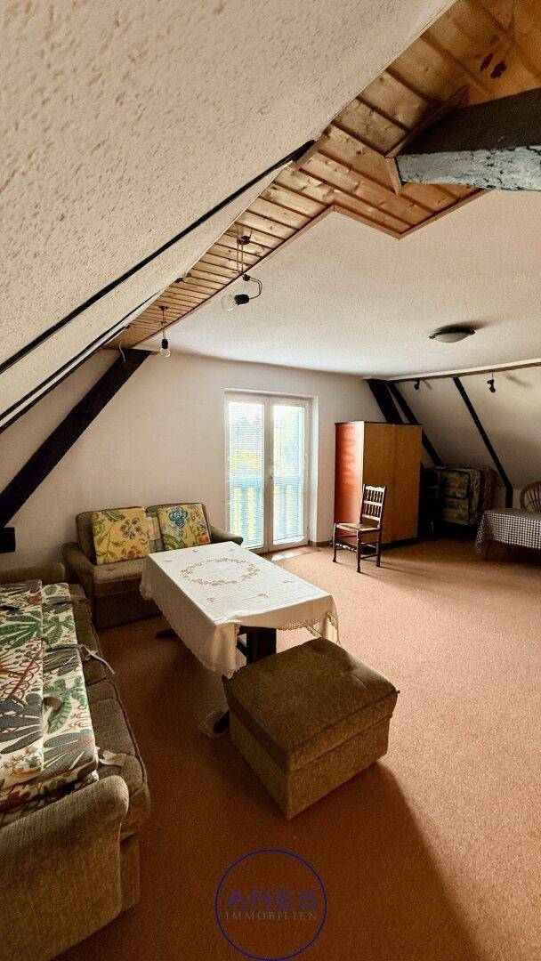 Gemütlicher Dachbodenraum mit Sitzgelegenheiten, Tisch und Zugang zu einem Balkon oder einer Terrasse.